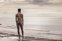 Visão traseira do jovem corredor feminino na praia olhando para o mar — Fotografia de Stock