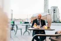 Mature businessman sitting outdoors at cafe, using laptop — Stock Photo