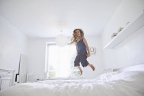 Молода дівчина стрибає на ліжку, низький кут зору — стокове фото