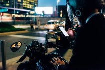 Reifer Geschäftsmann nachts mit Smartphone auf dem Motorrad — Stockfoto