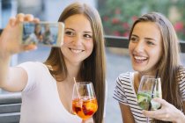 Two young female friends taking smartphone selfie at sidewalk cafe — Stock Photo