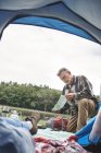 Reife Frau entspannt sich im Zelt, während der Mann draußen auf die Karte schaut — Stockfoto
