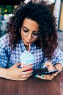 Женщина пользуется мобильным телефоном, наслаждаясь ледяным напитком — стоковое фото