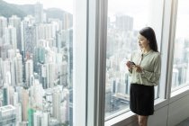 Бізнес-леді зі смартфоном, який дивиться з вікна — стокове фото