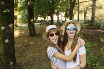 Retrato de dos amigas jóvenes en sombreros trilby sobresaliendo lenguas en el parque - foto de stock