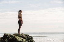 Молода жінка бігун стоячи на пляжі рок — стокове фото