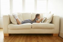 Молода дівчина лежить на дивані з цифровим планшетом — стокове фото