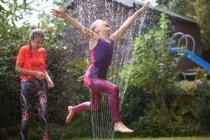 Ragazze che saltano sopra irrigatore giardino — Foto stock