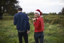 Vue arrière du jeune couple en chapeau de Père Noël et guirlande légère se promenant dans le champ — Photo de stock