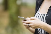 Captura recortada de mujer joven usando la pantalla táctil del teléfono inteligente en el parque - foto de stock