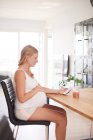 Vista laterale della donna incinta alla scrivania guardando lo smartphone — Foto stock