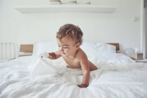 Toddler sitting on bed, holding unravelled toilet roll — Stock Photo