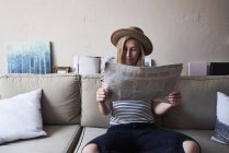 Mulher sentada no sofá, lendo jornal — Fotografia de Stock