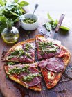 Sliced salami and pesto pizza on serving board, elevated view — Stock Photo
