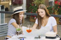 Two young female friends looking at map at sidewalk cafe — Stock Photo