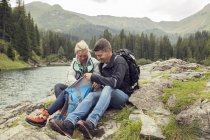 Coppia escursioni, seduto sul lago guardando smartphone, Tirolo, Steiermark, Austria, Europa — Foto stock