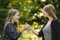 Duas jovens amigas dando aperto de mão secreto no parque — Fotografia de Stock