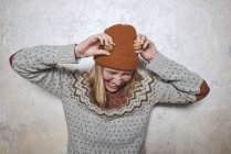 Портрет женщины в свитере и вязаной шляпе, держащей грецкие орехи на голове, смеющейся — стоковое фото