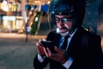 Reifer Geschäftsmann mit Motorradhelm nutzt nachts Smartphone — Stockfoto