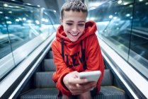 Breve dai capelli giovane donna che si muove giù scala mobile stazione della metropolitana guardando smartphone — Foto stock