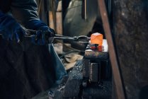 Gloved hands of blacksmith using tongs for red hot metal — Stock Photo