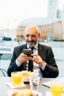 Зрілий бізнесмен використовує смартфон у відкритому кафе — стокове фото
