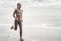 Jovem mulher correndo ao longo praia — Fotografia de Stock