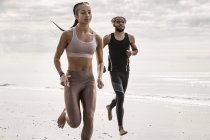 Молодой мужчина и женщина бегают босиком вдоль пляжа — стоковое фото
