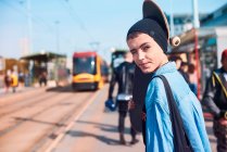 Ritratto di giovane skateboarder donna in cappello beanie alla stazione del tram — Foto stock