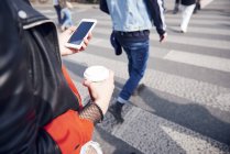 Person on pedestrian crossing with coffee and smartphone — Stock Photo