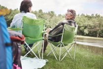 Pareja madura sentada en sillas de camping junto al lago - foto de stock
