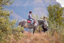 Chica montando a caballo en un entorno rural, madre caminando a su lado - foto de stock