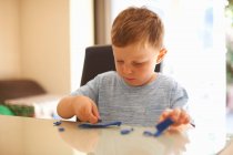 Мальчик, сидящий за столом и играющий с глиной — стоковое фото