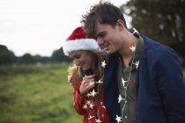 Giovane coppia in cappello di Babbo Natale e ghirlanda leggera in campo — Foto stock