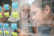 Three businesswomen behind glass wall pointing at adhesive notes — Stock Photo