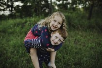 Retrato de menino dando a irmã um piggyback no campo — Fotografia de Stock