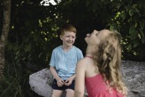 Girl sticking tongue out at brother sitting on rock — Stock Photo