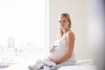 Portrait de jeune femme enceinte assise sur le lit — Photo de stock
