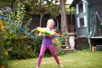 Chica chorreando pistola de agua en el jardín - foto de stock