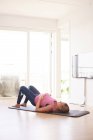 Беременная молодая женщина тренируется на коврике для йоги в гостиной — стоковое фото