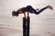 Jovem fazendo suporte de mão em postes de praia de madeira — Fotografia de Stock
