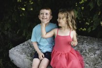 Girl with hand on brother's chin, sitting on rock — Stock Photo