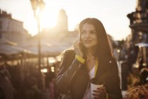Junge Frau geht im Freien, hält Kaffeetasse, benutzt Smartphone, Tätowierungen an Händen und Hals — Stockfoto