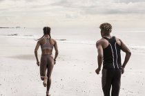 Rear view of young male and female running on beach — Stock Photo