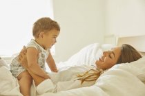 Mother relaxing on bed with toddler, smiling — Stock Photo