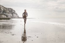 Vue de face de la jeune coureuse courant pieds nus le long de la plage — Photo de stock