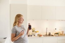 Mujer joven embarazada en la cocina con botella de jugo de frutas - foto de stock