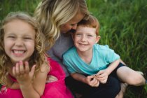 Portrait of girl and brother sitting on mothers lap in grass — Stock Photo