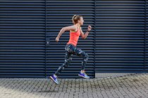 Young female runner speed running along sidewalk — Stock Photo
