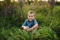 Retrato de menino sorridente sentado na grama alta olhando para a câmera — Fotografia de Stock